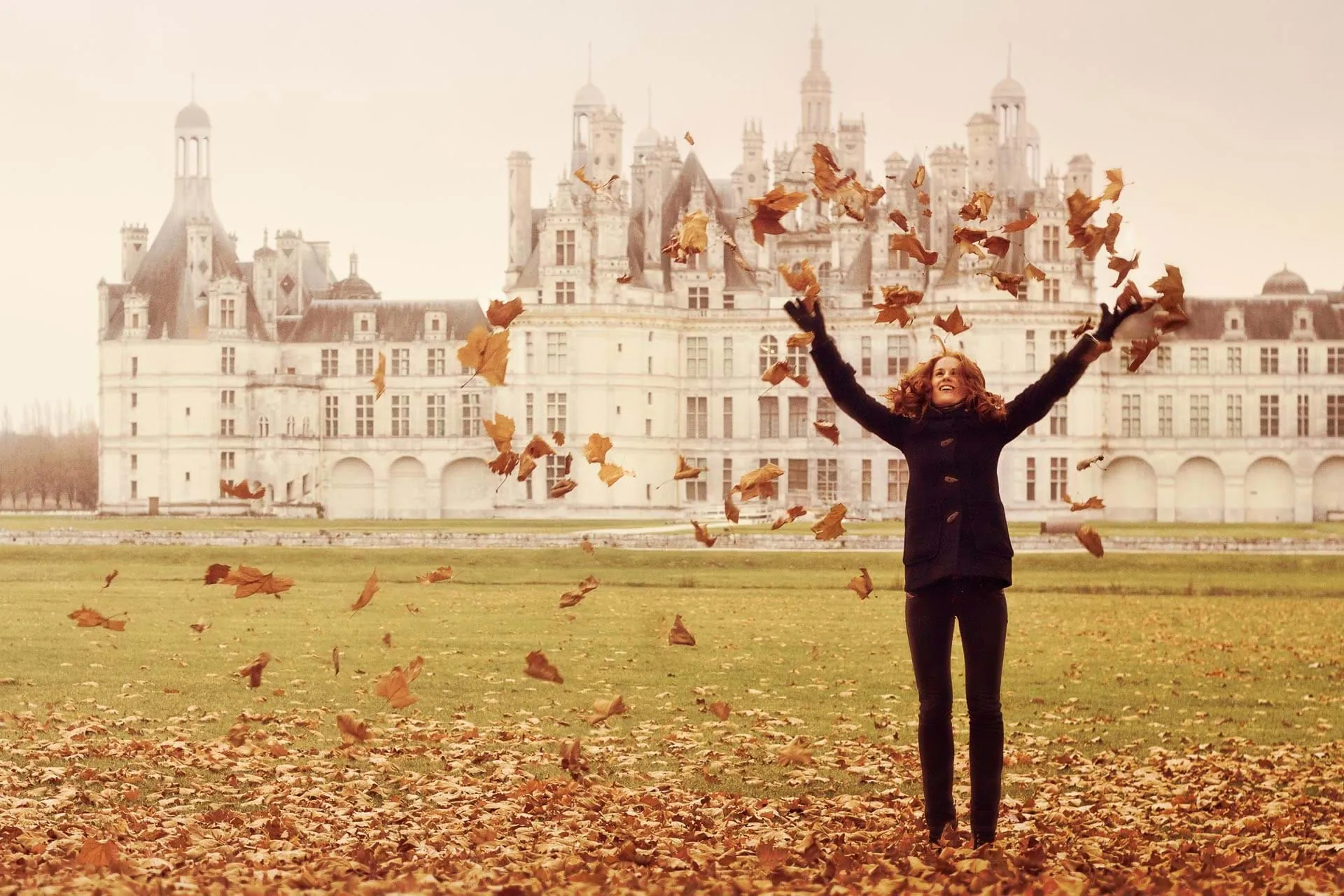 Woman throwing autumn leaves into the air in front of Château de Chambord