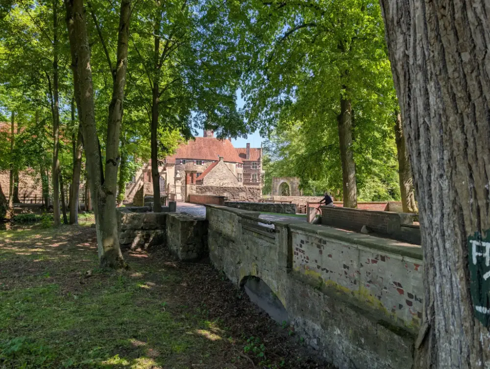 Schattiger Waldweg mit alten Mauern, im Hintergrund die Burg Vischering in Lüdinghausen